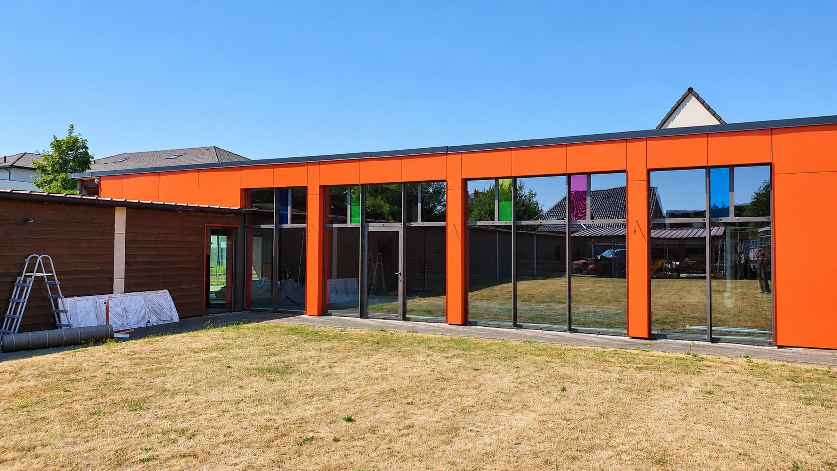 Bâtiment à façade orange percée de grandes baies vitrées, échelle posée contre le mur