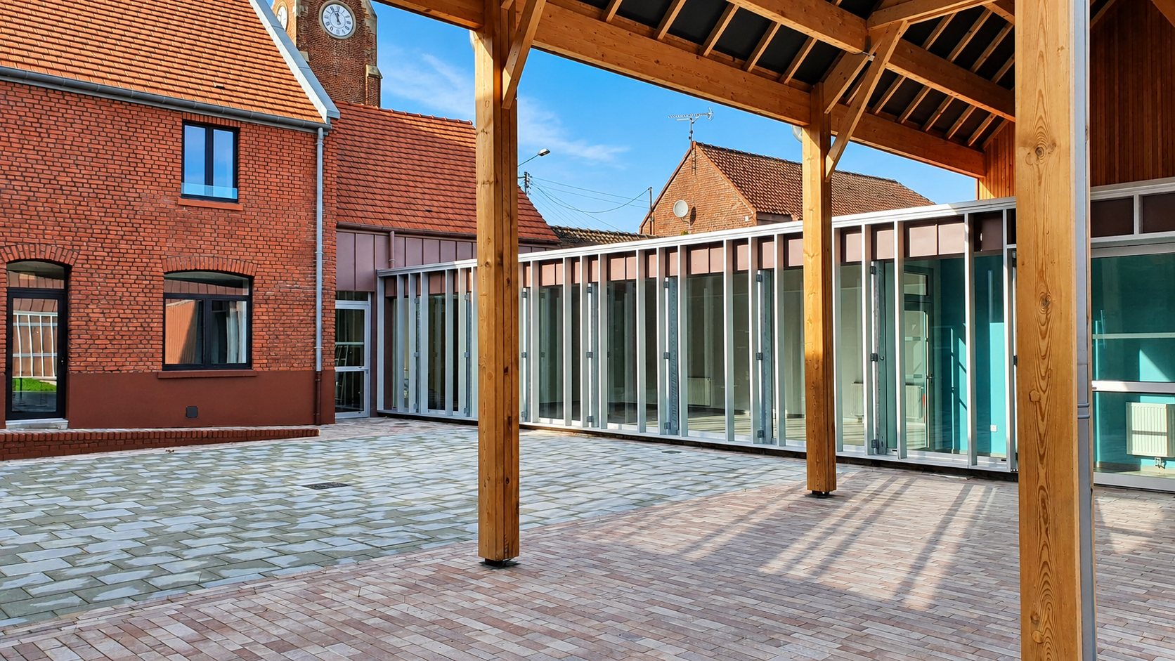 Façade vitrée sur une cour pavée, sous une charpente en bois