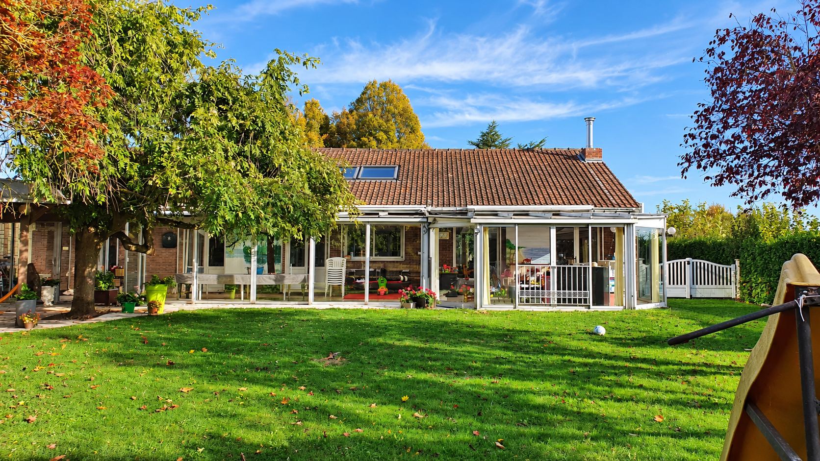 Longue véranda blanche vitrée au bout d'un jardin